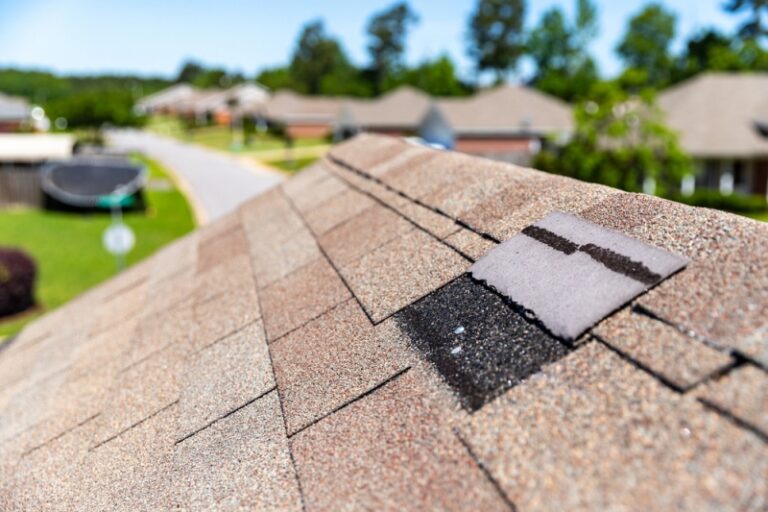 A closeup of a roof with brown shingles. You can see that one of the center shingles is missing, leaving a black square in its place.