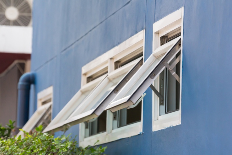 A blue wall of a house with three open awning windows lined up in a row.