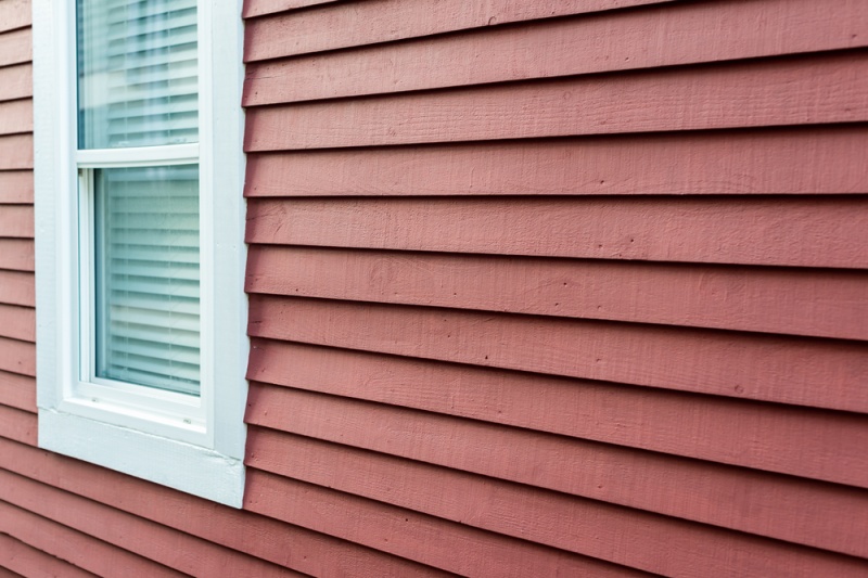A close up of a home's exterior painted red with a double-hung window off to the left side.
